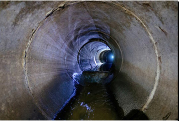 Large concrete sewer tunnel with water and light down the line