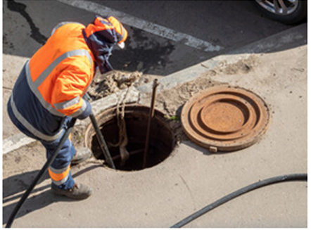 Hi-vis worker beside an open manhole doing drain maintenance